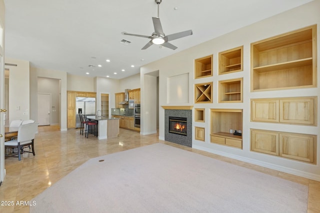 living room with built in shelves, a tile fireplace, recessed lighting, visible vents, and baseboards