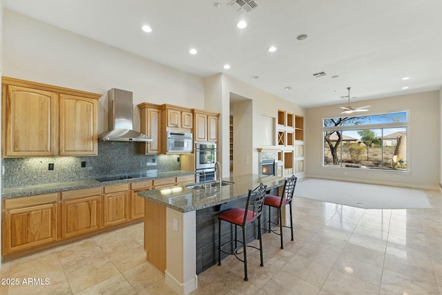 kitchen with a breakfast bar, visible vents, wall chimney range hood, appliances with stainless steel finishes, and an island with sink