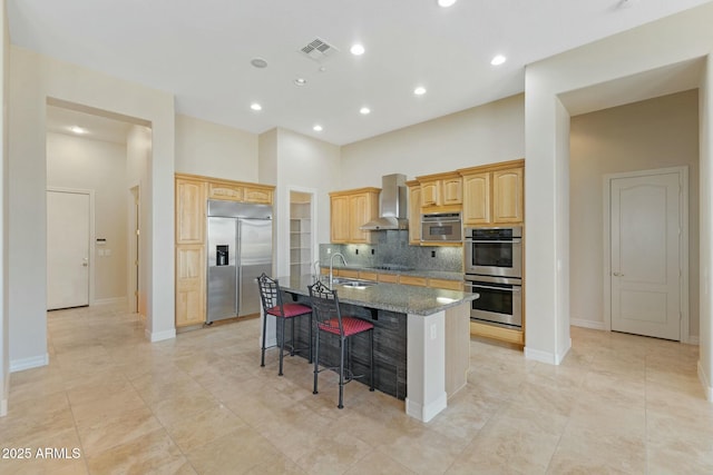 kitchen featuring appliances with stainless steel finishes, a breakfast bar, a kitchen island with sink, wall chimney range hood, and a sink