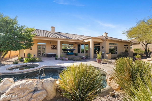 back of house with an in ground hot tub, a chimney, a ceiling fan, and stucco siding