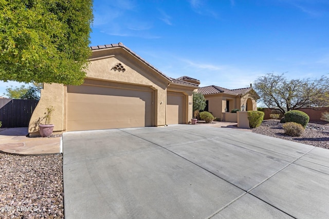 mediterranean / spanish-style home with a tile roof, stucco siding, concrete driveway, fence, and a garage