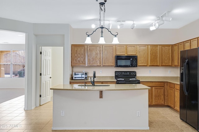 kitchen featuring a toaster, a sink, black appliances, a center island with sink, and pendant lighting