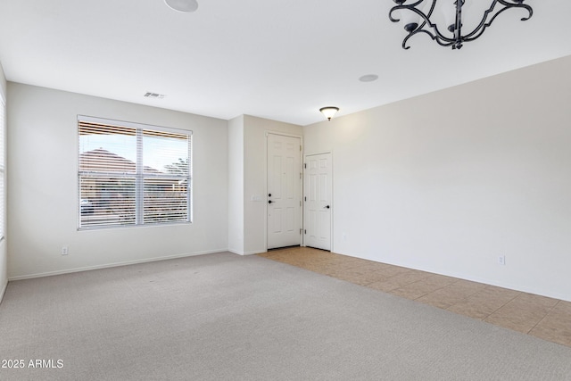 spare room with an inviting chandelier, carpet flooring, visible vents, and baseboards