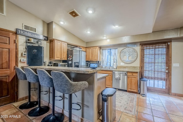 kitchen featuring appliances with stainless steel finishes, lofted ceiling, sink, a kitchen bar, and light tile patterned floors