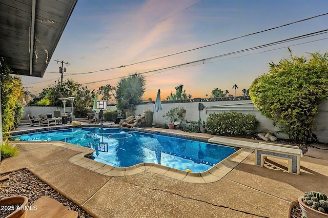 pool at dusk featuring a diving board and a patio area