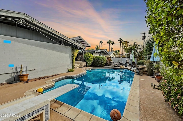 pool at dusk featuring a patio and a diving board