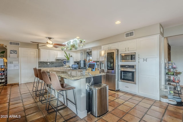 kitchen with appliances with stainless steel finishes, a kitchen breakfast bar, light stone counters, tasteful backsplash, and white cabinets