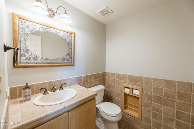 half bath with tile walls, visible vents, vanity, and toilet