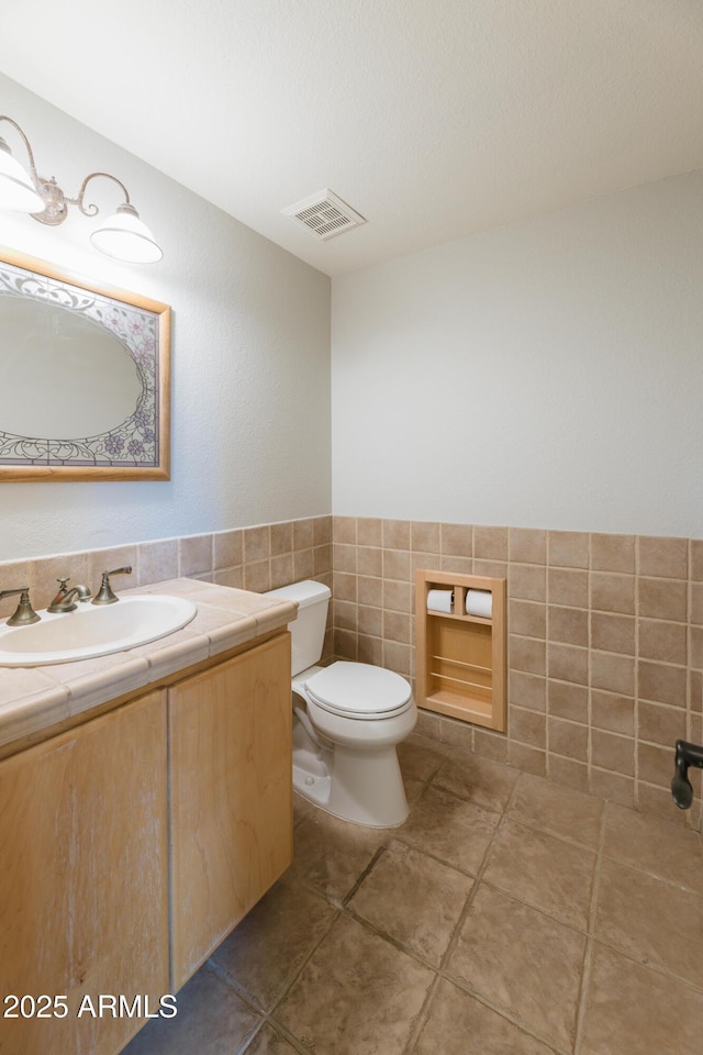 bathroom with visible vents, toilet, tile patterned floors, vanity, and tile walls