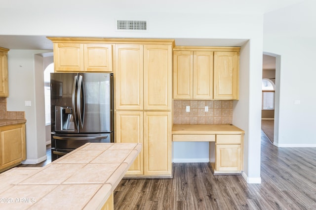 kitchen featuring visible vents, stainless steel refrigerator with ice dispenser, tile counters, decorative backsplash, and light brown cabinetry