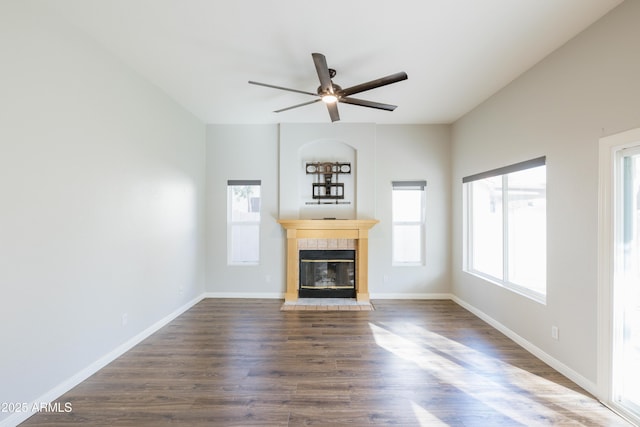 unfurnished living room featuring dark wood-style floors, ceiling fan, a tile fireplace, and baseboards