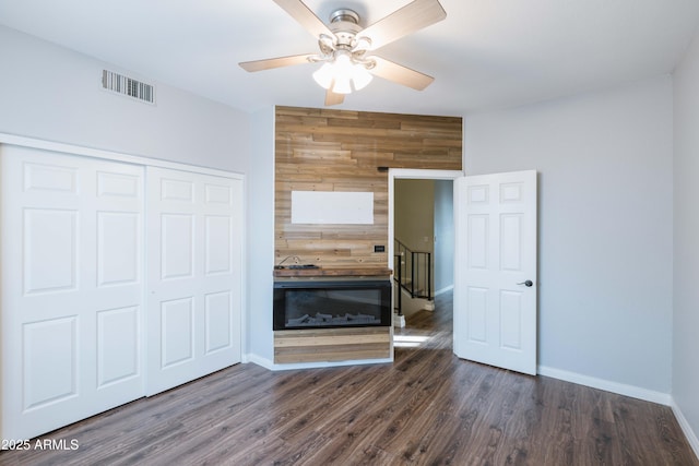 unfurnished bedroom with dark wood-type flooring, a closet, visible vents, and wooden walls