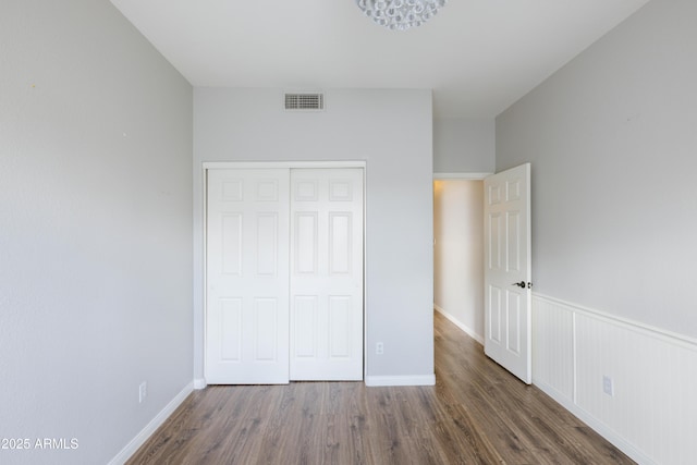 unfurnished bedroom featuring baseboards, visible vents, wainscoting, wood finished floors, and a closet