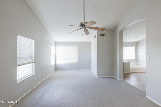 carpeted empty room with a ceiling fan, arched walkways, visible vents, and baseboards