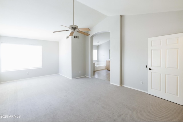 carpeted empty room featuring arched walkways, visible vents, baseboards, vaulted ceiling, and a ceiling fan