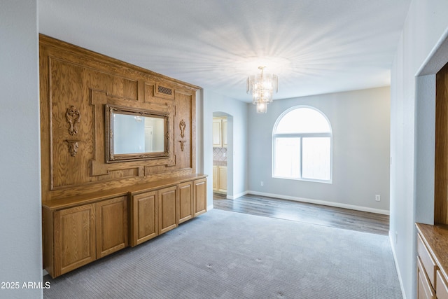 interior space featuring a chandelier, arched walkways, light colored carpet, and baseboards