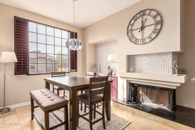 dining space featuring baseboards, a notable chandelier, a tiled fireplace, and light tile patterned floors