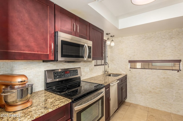 kitchen featuring light stone counters, light tile patterned flooring, stainless steel appliances, a sink, and reddish brown cabinets