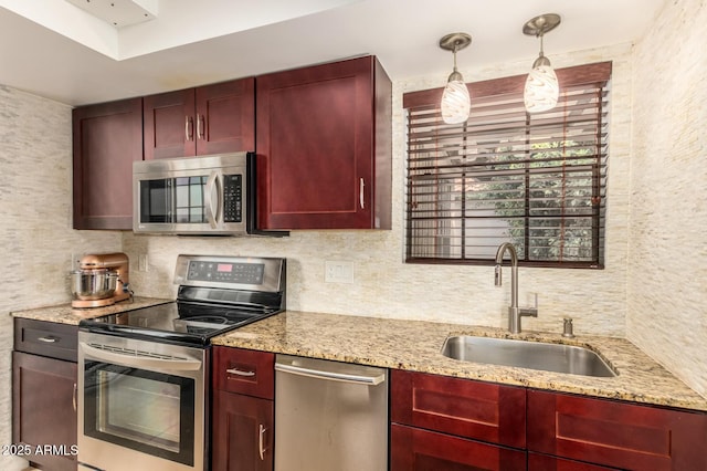 kitchen with appliances with stainless steel finishes, reddish brown cabinets, a sink, and hanging light fixtures