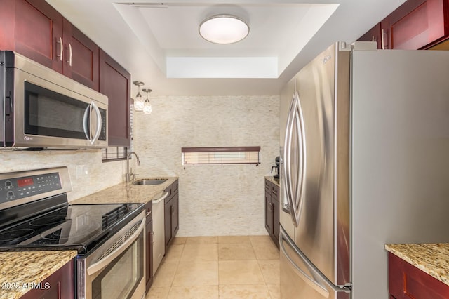 kitchen with appliances with stainless steel finishes, reddish brown cabinets, a sink, and light stone counters