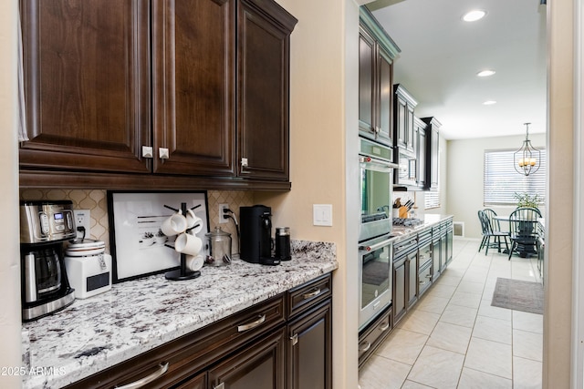 kitchen with decorative backsplash, light stone countertops, dark brown cabinetry, and pendant lighting