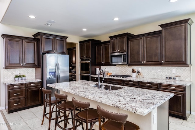 kitchen featuring appliances with stainless steel finishes, a breakfast bar area, dark brown cabinetry, sink, and a kitchen island with sink