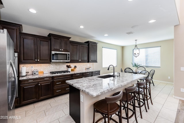 kitchen featuring appliances with stainless steel finishes, sink, a kitchen bar, decorative light fixtures, and an island with sink