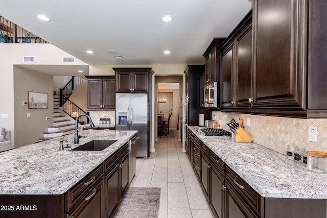 kitchen featuring dark brown cabinets, stainless steel appliances, backsplash, sink, and a kitchen island with sink