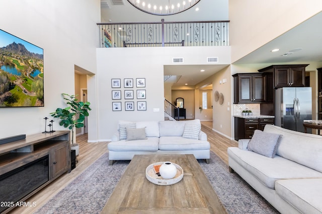 living room with light hardwood / wood-style floors, an inviting chandelier, and a towering ceiling