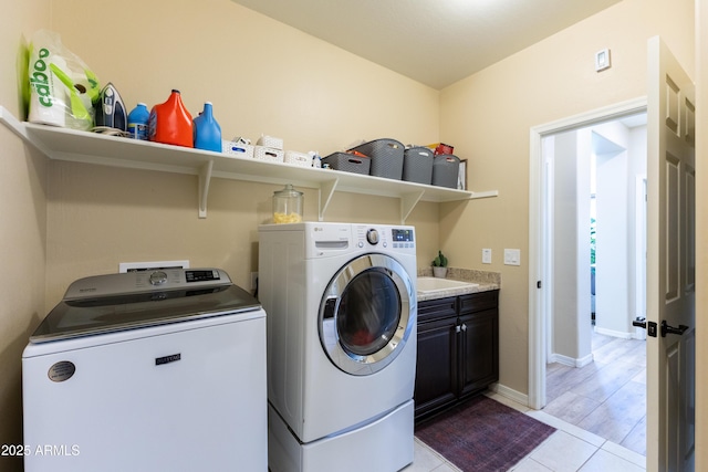 laundry room featuring light tile patterned floors, separate washer and dryer, and cabinets