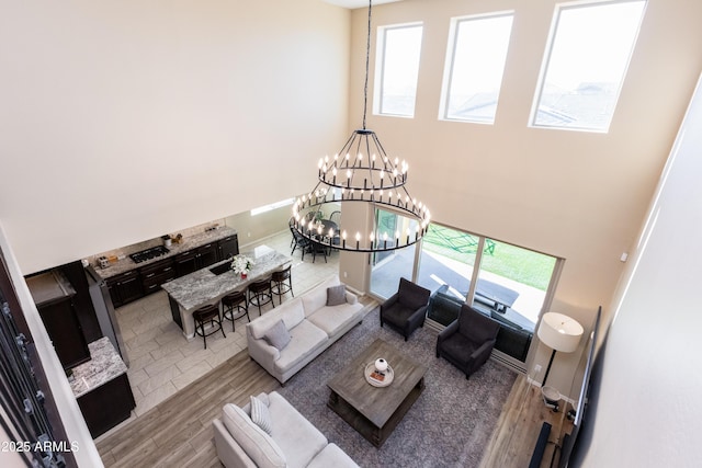 living room featuring light wood-type flooring, a towering ceiling, an inviting chandelier, and a wealth of natural light