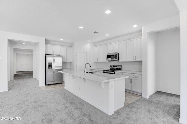 kitchen with stainless steel appliances, light carpet, a sink, white cabinetry, and a kitchen bar