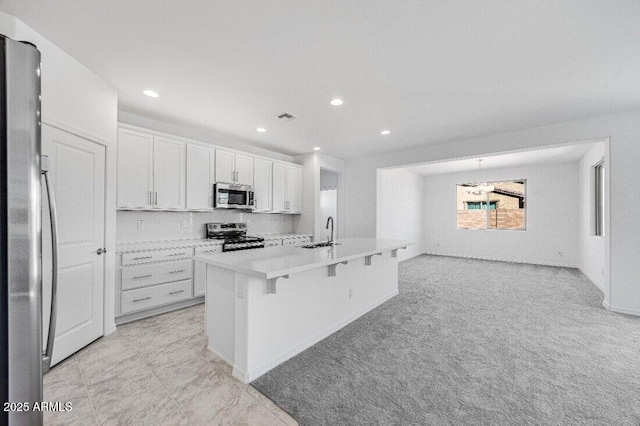 kitchen featuring a breakfast bar area, light countertops, appliances with stainless steel finishes, a kitchen island with sink, and white cabinetry