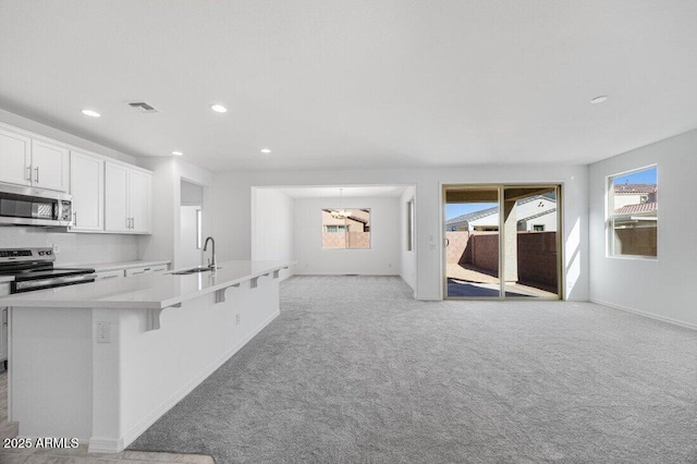 kitchen featuring visible vents, a kitchen island with sink, stainless steel appliances, light countertops, and a sink