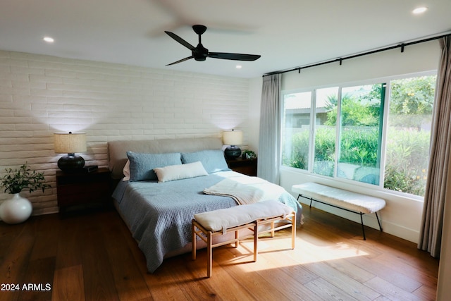 bedroom featuring hardwood / wood-style floors, ceiling fan, and brick wall