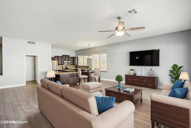 living room featuring ceiling fan with notable chandelier and light hardwood / wood-style flooring