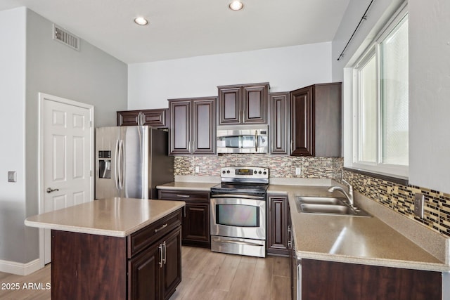 kitchen with a center island, sink, appliances with stainless steel finishes, dark brown cabinets, and light hardwood / wood-style floors