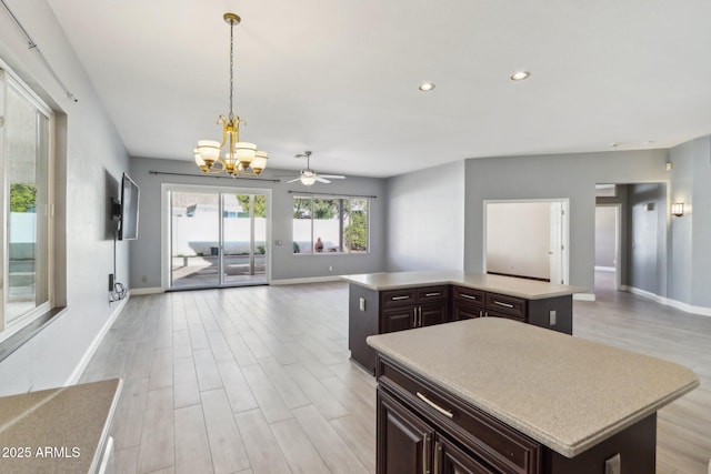 kitchen with hanging light fixtures, light hardwood / wood-style flooring, dark brown cabinets, a kitchen island, and ceiling fan with notable chandelier