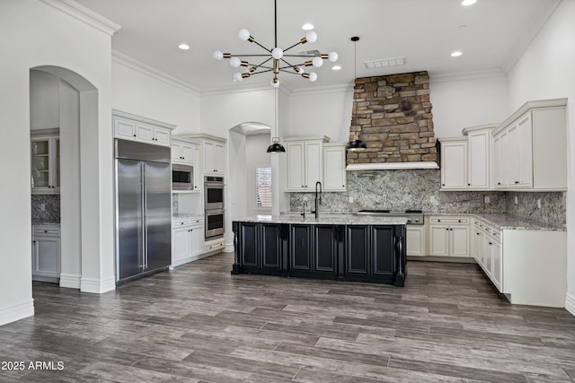 kitchen featuring tasteful backsplash, a center island with sink, visible vents, built in appliances, and pendant lighting