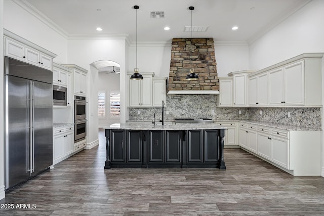 kitchen with pendant lighting, visible vents, a center island with sink, and built in appliances