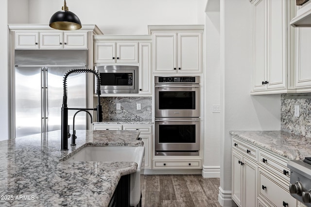 kitchen featuring built in appliances, light stone counters, dark wood-style flooring, and decorative backsplash