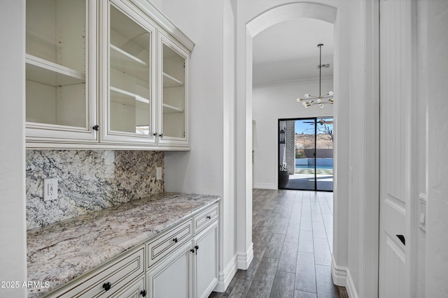 bar featuring arched walkways, baseboards, dark wood-style floors, crown molding, and backsplash