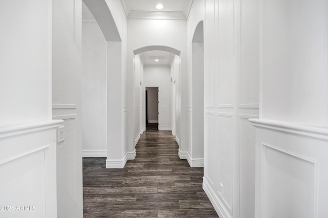 corridor with arched walkways, recessed lighting, baseboards, ornamental molding, and dark wood finished floors