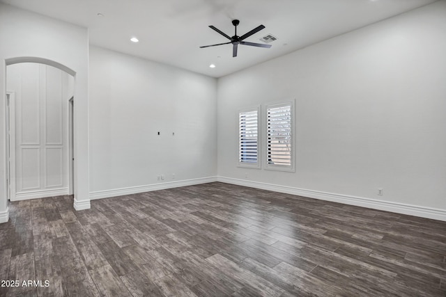 empty room with arched walkways, ceiling fan, dark wood finished floors, and baseboards