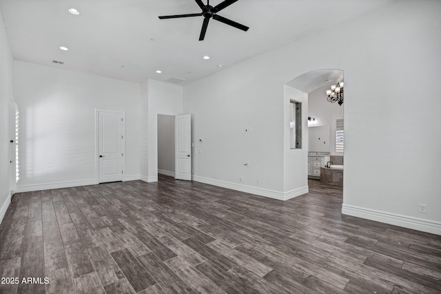 unfurnished living room with arched walkways, recessed lighting, ceiling fan with notable chandelier, dark wood-type flooring, and baseboards