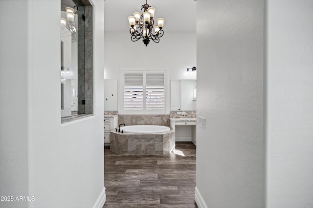 bathroom featuring wood finished floors, a notable chandelier, baseboards, and a bath