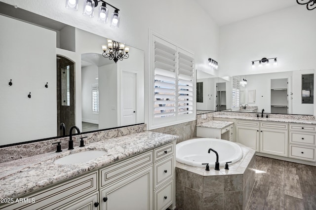 full bath with a bath, two vanities, a sink, and wood finished floors