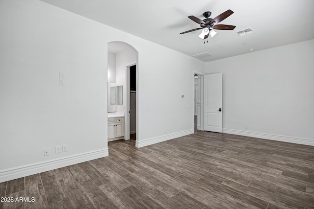 unfurnished bedroom featuring baseboards, visible vents, arched walkways, and dark wood-type flooring