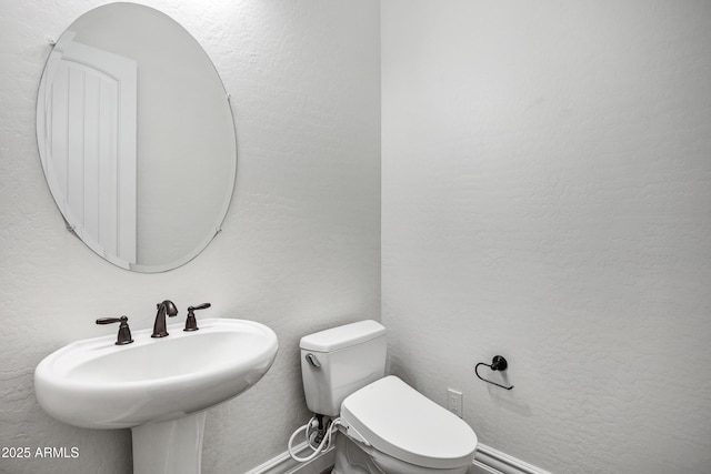 bathroom featuring toilet, a sink, and a textured wall