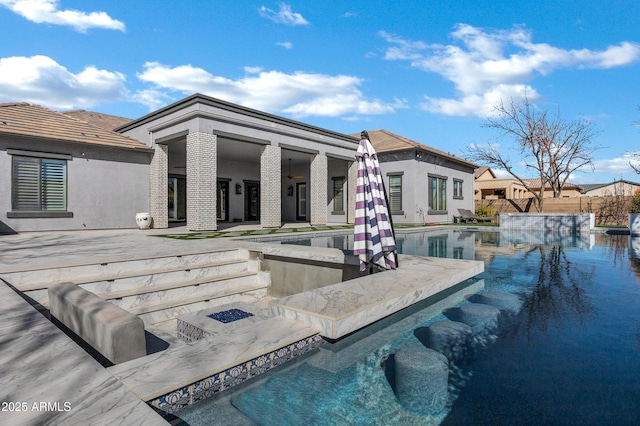 rear view of property with stucco siding, an outdoor pool, a hot tub, and ceiling fan